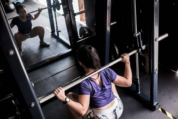 Een atletisch Aziatisch meisje doet volledige kraakpanden op een smid machine. Trainen en trainen in de fitnessruimte of fitnessclub. - Foto, afbeelding