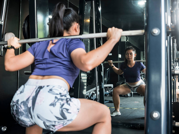 A fit asian girl does some full squats on a smith machine. Working out and training at the gym or fitness club. - Photo, Image