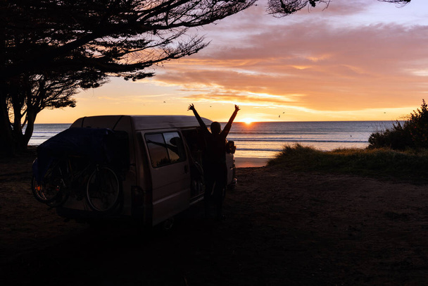 Joven despertando al amanecer junto a la playa junto a su caravana. Concepto Van Life. - Foto, Imagen