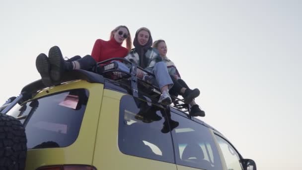 Three the best girlfriends sits on yellow car outdoors and poses on camera - Footage, Video