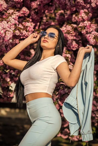 Passionate about spring. Clothes shop. Gorgeous fancy girl outdoors. Woman fancy sunglasses in spring flower bloom. Girl in cherry blossom flower. Spring fashion collection. Sakura tree blooming - Φωτογραφία, εικόνα