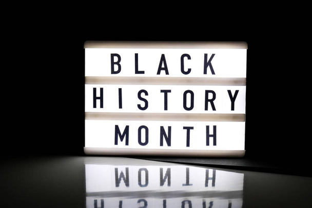 Caja de luz con texto MES DE HISTORIA NEGRO sobre fondo negro oscuro con reflejo espejo. Mensaje evento histórico. Luz - Foto, imagen