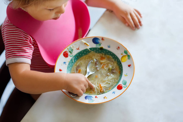 Close-up baby meisje eten van lepel groente noodle soep. voeding, kind, voeding en ontwikkeling. close-up van peuter, dochter met lepel zitten in de kinderstoel en leren eten door zelf - Foto, afbeelding