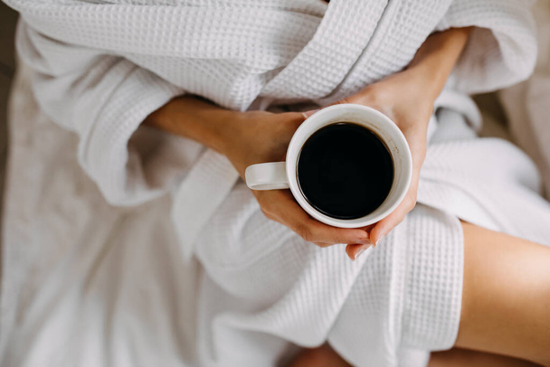 cropped shot of woman in white bathrobe with cup of coffee relaxing at home - Photo, Image
