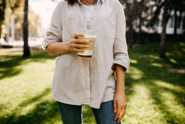 levágott lövés a nő műanyag csésze latte pihentető fű a parkban - Fotó, kép