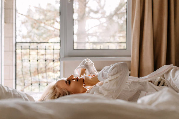 όμορφη νεαρή γυναίκα με πιτζάμες χαλαρώνοντας στο κρεβάτι το πρωί - Φωτογραφία, εικόνα