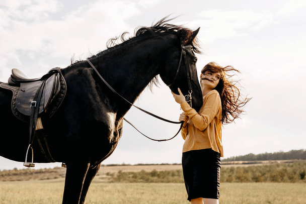 portret van mooie vrouw met zwart paard in de natuur - Foto, afbeelding