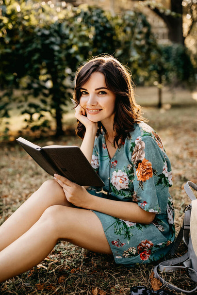portrait of beautiful young woman reading book on grass in park - Photo, Image