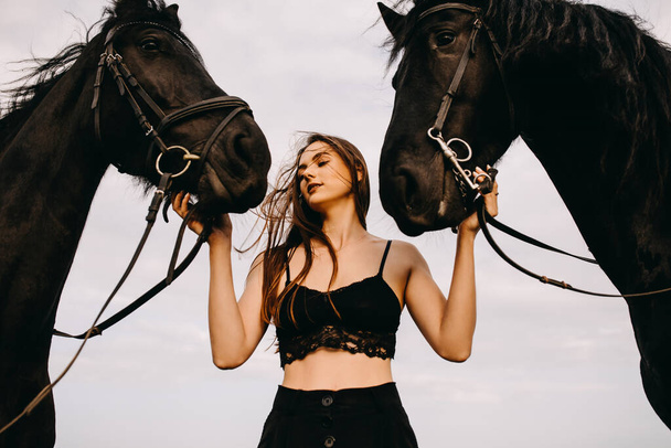 portrait of beautiful woman in black dress with two horses in nature - Фото, изображение