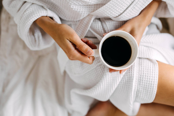 tiro recortado de mujer en albornoz blanco con taza de café relajante en casa - Foto, imagen