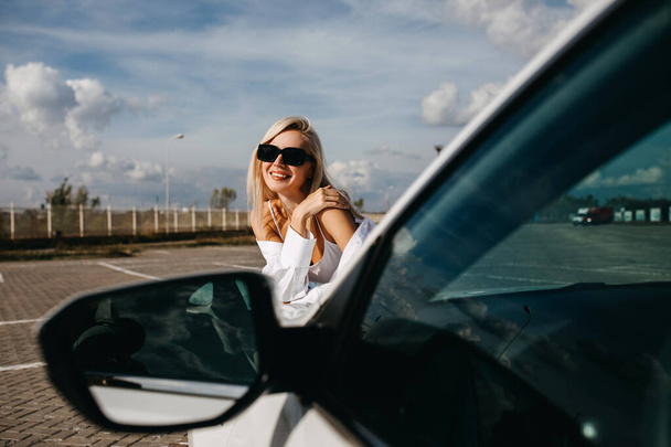 όμορφη νεαρή γυναίκα ακουμπά στο αυτοκίνητό της στο πάρκινγκ - Φωτογραφία, εικόνα