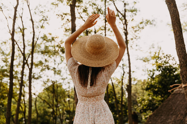 rear view of woman in dress and straw hat in forest - Photo, Image