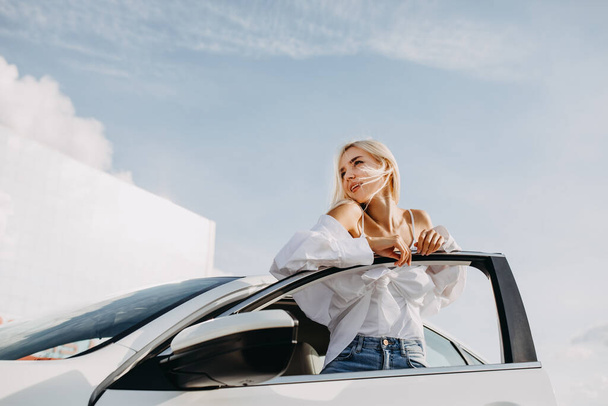 beautiful young woman standing in front of her car on parking - 写真・画像