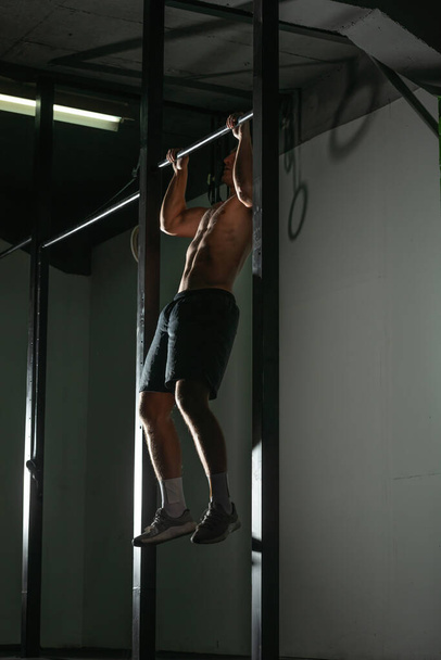Handsome bodybuilder doing pull-ups on horizontal bar in a indoors modern gym. - Foto, Imagen