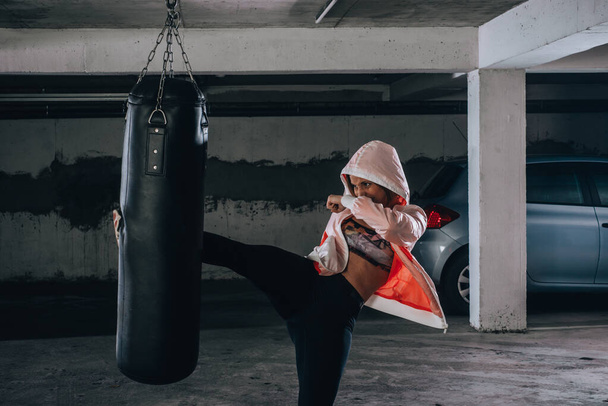 Fiatal sportoló csinál magas rúgás közben boksz gyakorlat egy garázsban. - Fotó, kép