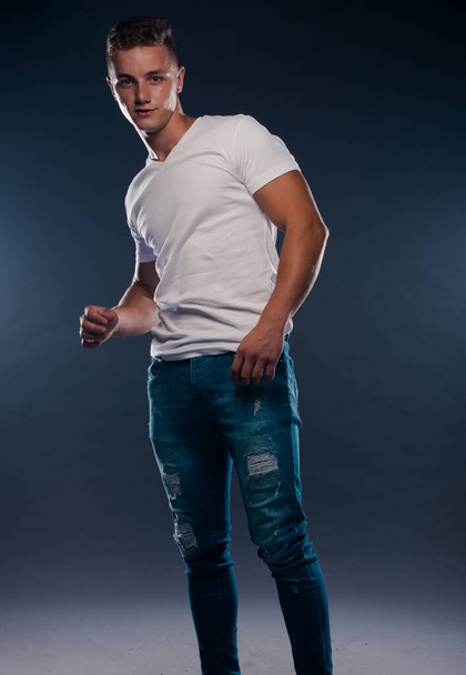 Portrait of a young attractive man dressed in blue ripped jeans and sneakers - Photo, Image