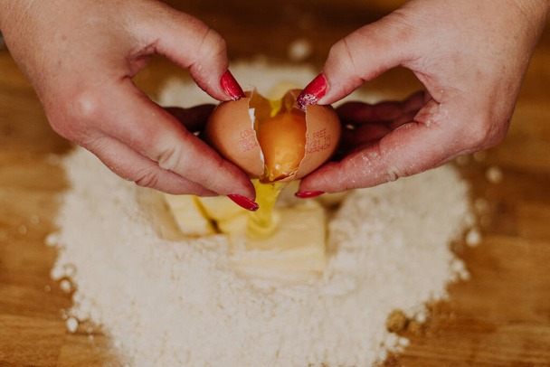 A closeup of a woman cracking an egg on flour with sliced butter to make cookies - 写真・画像