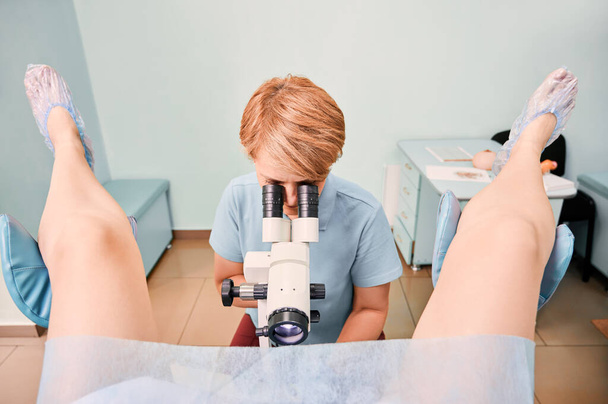 Doctor examining woman with colposcope in gynecological clinic. Patient sitting in gynecological chair while gynecologist doing colposcopy examination. Concept of gynecology and female health. - Photo, Image