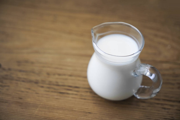 fresh milk in glasses jug on wooden board background. empty copy space for insription. - 写真・画像