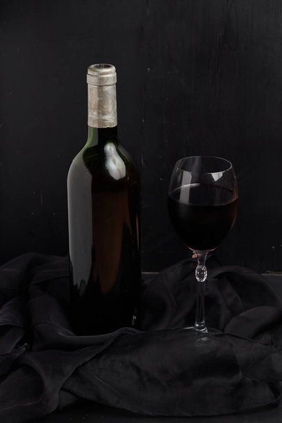 A vertical shot of a bottle of wine and a wineglass by a black background - Foto, Bild