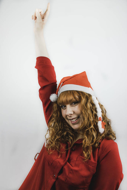 A happy young female in a funny Santa hat pointing up with a forefinger - Fotó, kép