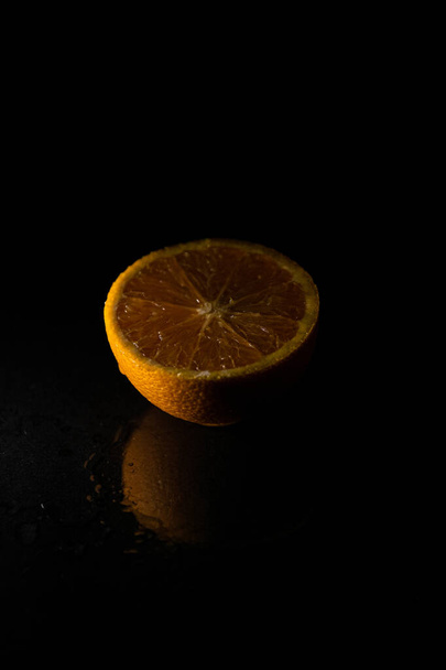 A vertical closeup of a sliced orange isolated on a black background - Фото, изображение