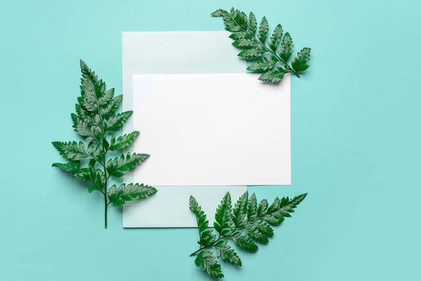Blanco vel papier en groene bladeren op achtergrond kleur - Foto, afbeelding