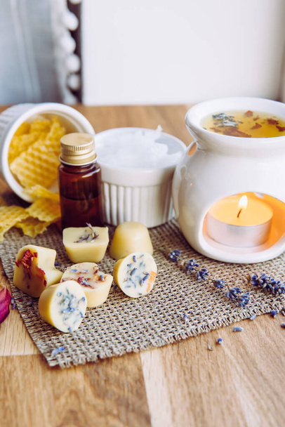 Using homemade mini wax melts in aromatherapy lamp diffuser at home interior concept. Melts making ingredients on table for unbleached beeswax, solid coconut oil, essential oil, dried flowers. - Фото, изображение