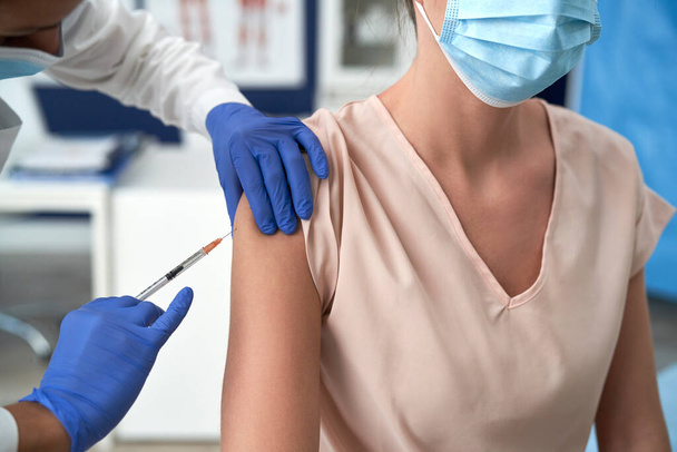 Vrouw met gezichtsmasker wordt gevaccineerd                                - Foto, afbeelding