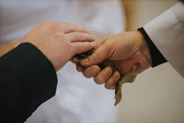 A closeup shot of groom and priest hands on a cross - Zdjęcie, obraz