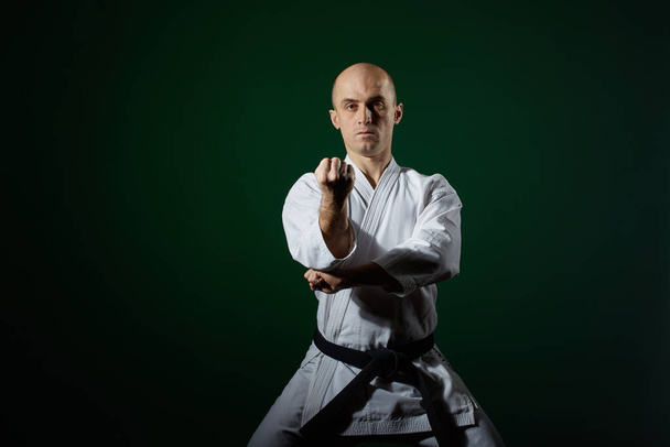 Karategissa urheilija kouluttaa muodollisia karateharjoituksia tummanvihreällä taustalla. - Valokuva, kuva
