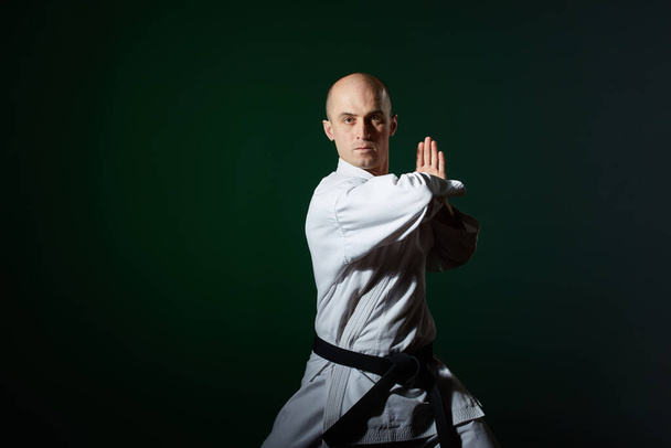 Op een donkergroene achtergrond, een atleet in karategi maakt formele karate oefeningen - Foto, afbeelding