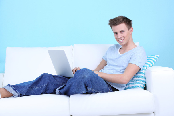 Guy lie on sofa with laptop on blue background - 写真・画像