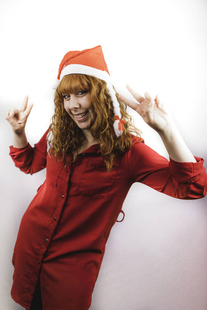 A smiling young female in a red Santa hat posing with two fingers up - Fotó, kép
