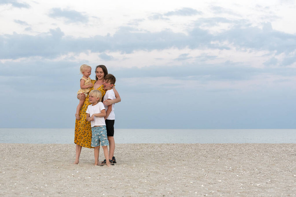 Onnellinen perhe rannalla. Äiti ja kolme lasta pitävät hauskaa merellä. Perheen elämäntapa - Valokuva, kuva