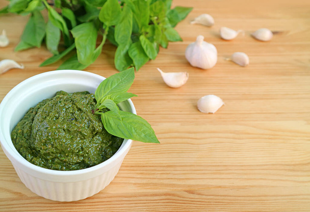 Bowl of Homemade Fresh Basil Pesto Sauce with Blurry Ingredients on Wooden Background - Photo, Image