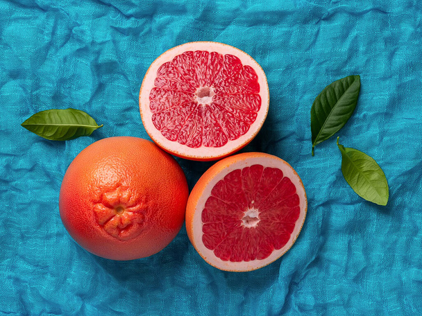 Whole ripe grapefruit and two juicy halves on a turquoise cloth background. Ingredient for fruit desserts. Tasty vegetarian food, slimming diet and vitamin healthy eating. Top view.  - Zdjęcie, obraz