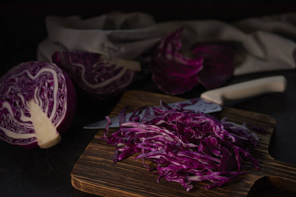 A closeup of cut red cabbage with a knife on a wooden board against a dark background - Valokuva, kuva