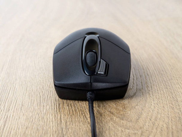 Close-up of black wired optical mouse over brown desk. Work or study at the computer at home or in the office. Front view. - Fotoğraf, Görsel