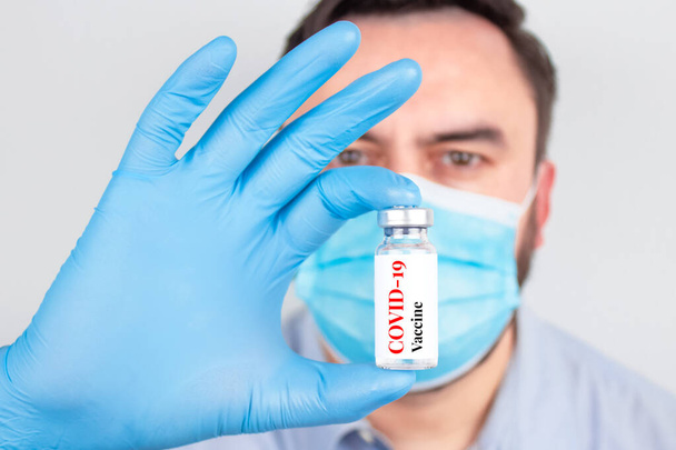Doctor or scientist wearing medical face mask and holding COVID-19 vaccine - coronavirus prevention, global vaccination concept, selective focus - Photo, Image