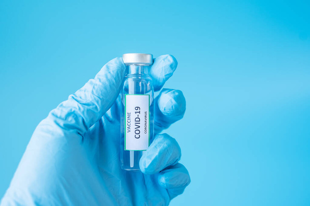 COVID-19 Vaccin injectieflacon tegen Coronavirus infectie in de hand van een arts met Nitril Glove in het ziekenhuis laboratorium. Medisch, gezondheids-, vaccinatie- en immunisatieconcept - Foto, afbeelding