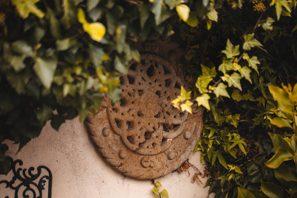 A closeup shot of a stone clock sculpture outside of a house surrounded by trees and bushes - Zdjęcie, obraz