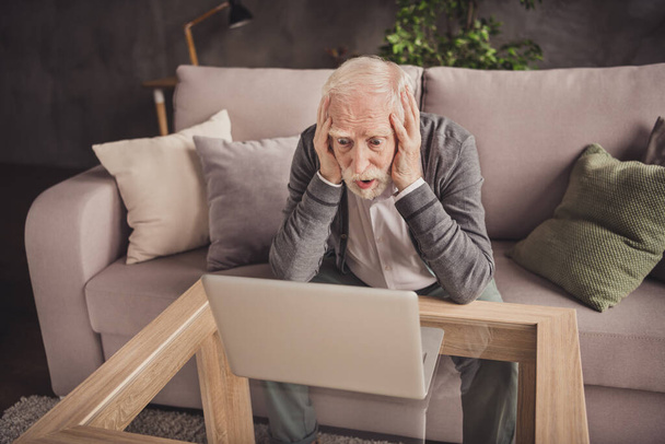 Photo of depressed pensioner wear grey cardigan sitting arms head watching modern gadget indoors house flat - Foto, imagen