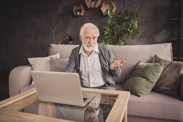 Beyaz gömlekli komik yaşlı adamın fotoğrafı kanepeye oturmuş iletişim kuran modern aletleri ev içinde gösteriyor. - Fotoğraf, Görsel