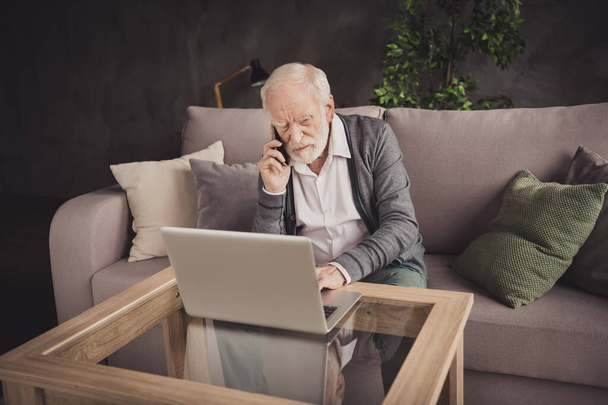 Photo of angry pensioner wear grey cardigan sitting looking modern gadget talking phone indoors house flat - Photo, Image