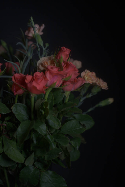 黒い背景に赤い小さなバラとオレンジのカーネーションの花束。 - 写真・画像
