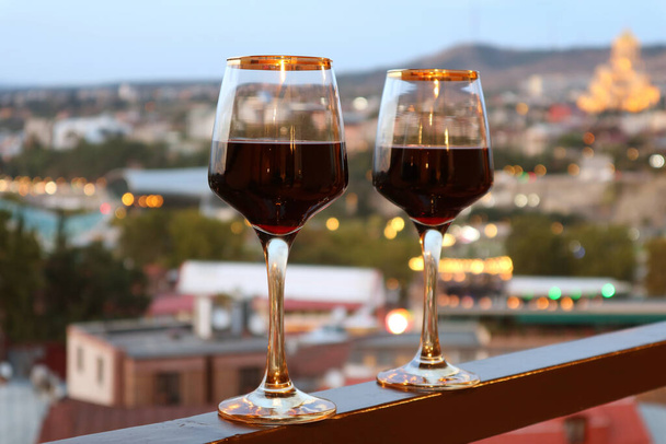 Twee wijnglazen op het balkon met wazig avondzicht op de stad in de achtergrond - Foto, afbeelding