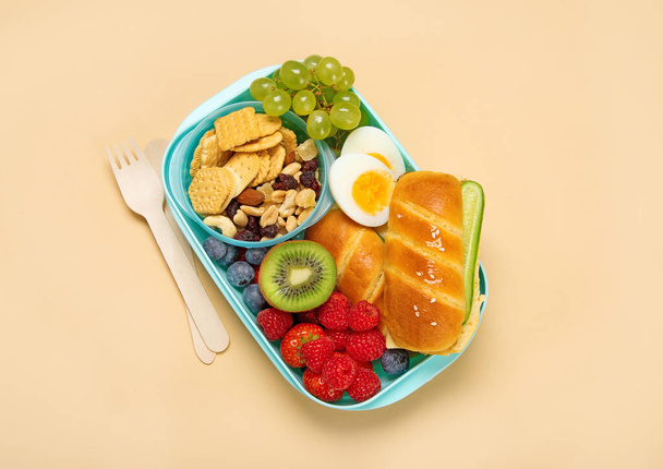 Школьная обеденная коробка с бутербродами, овощами и фруктами на оранжевом фоне. Вид сверху - Фото, изображение