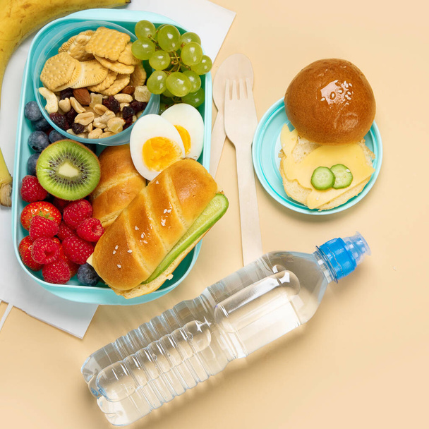 School lunch box with sandwiches, vegetables and fruits on orange background. Top view, copy space - Photo, image