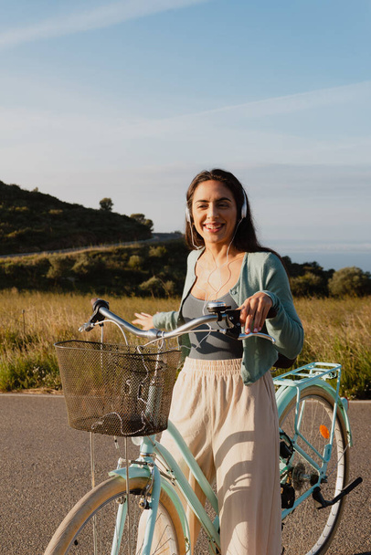 ライトブルーの自転車に乗ってヘッドフォンで音楽を聞いて笑顔の白い女性 - 写真・画像